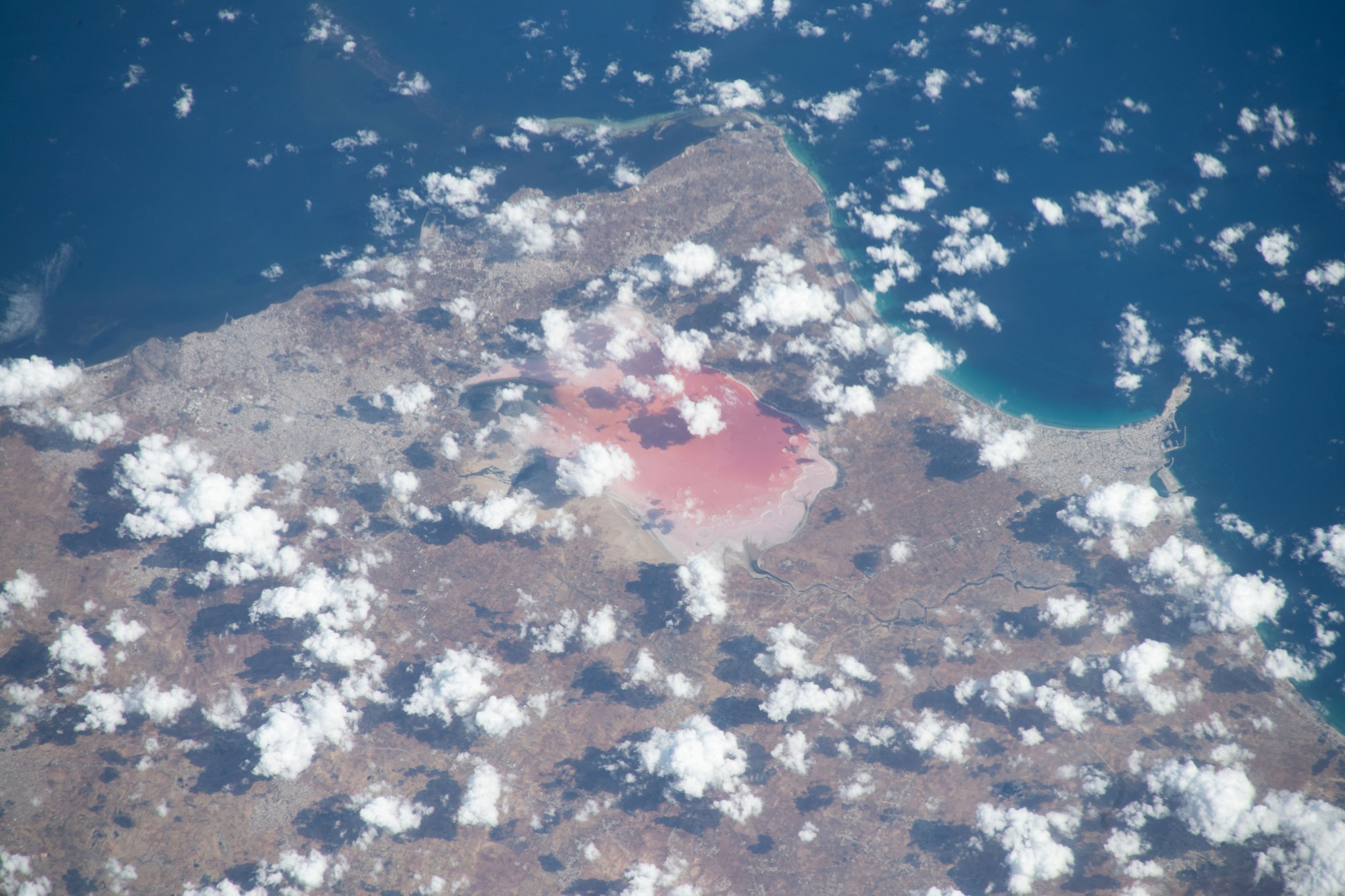 iss070e002574 (Oct. 7, 2023) -- Clouds hover around the coast of Tunisia as the International Space Station soars 260 miles above. Near the center peak where the coastline meets the Mediterranean Sea, the pink salt lake of Sebkha of Moknine is visible. With little inflow from rivers and streams, the lake is fed by rainfall which flushes vibrant colors into the basin, leaving behind remnants of a "salt pan," the white crust of salt and minerals bordering the water.