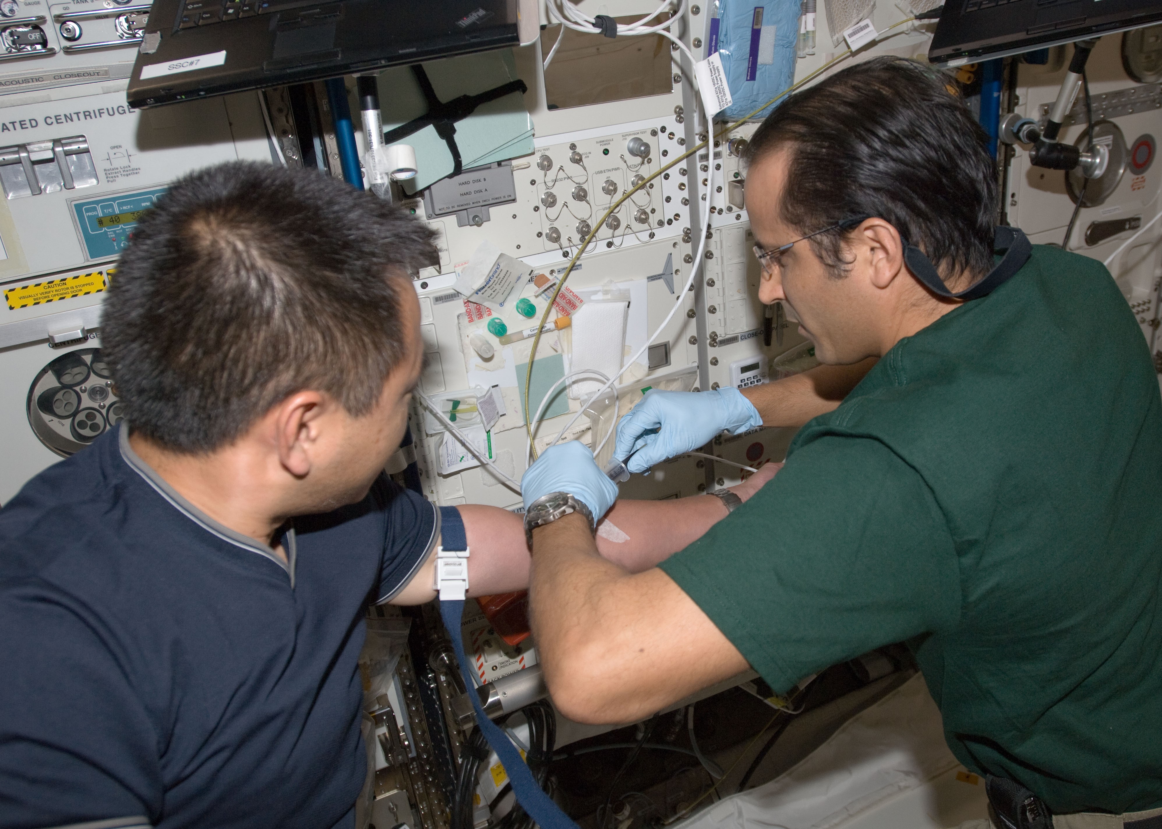 NASA astronaut Joseph M. Acaba drawing a blood sample from Akihiko Hoshide of the Japan Aerospace Exploration Agency