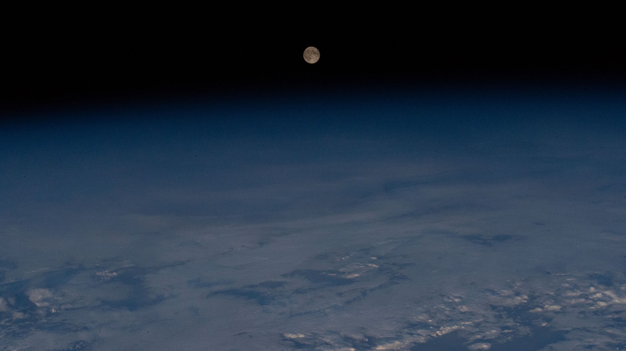 iss070e001502 (Sept. 30, 2023) -- September's Harvest Moon can be seen from the International Space Station as it soared 260 miles above the Northwestern coast of Canada. A few scatters of clouds can be seen hovering over Earth, while the Moon centers itself above.
