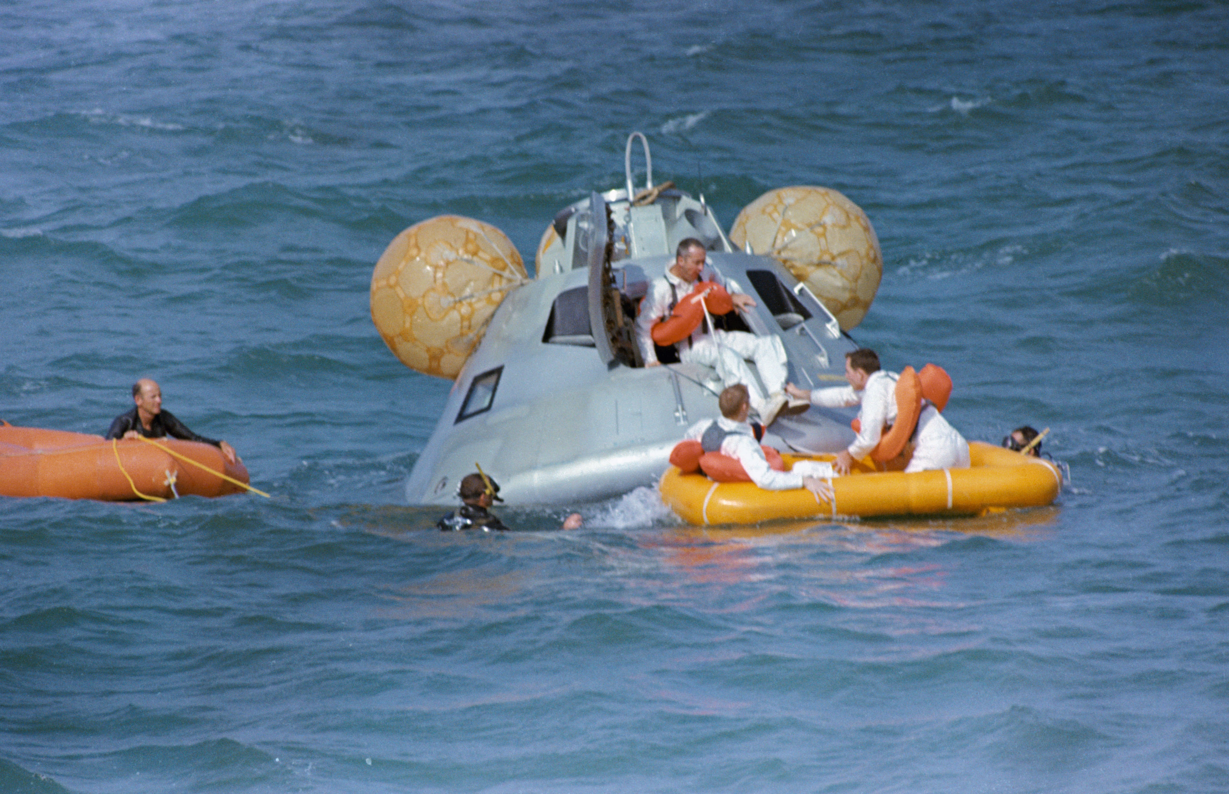 Photo of McDivitt, emerging from the CM, Schweickart, at left in the raft, and Scott complete water egress training in the Gulf of Mexico