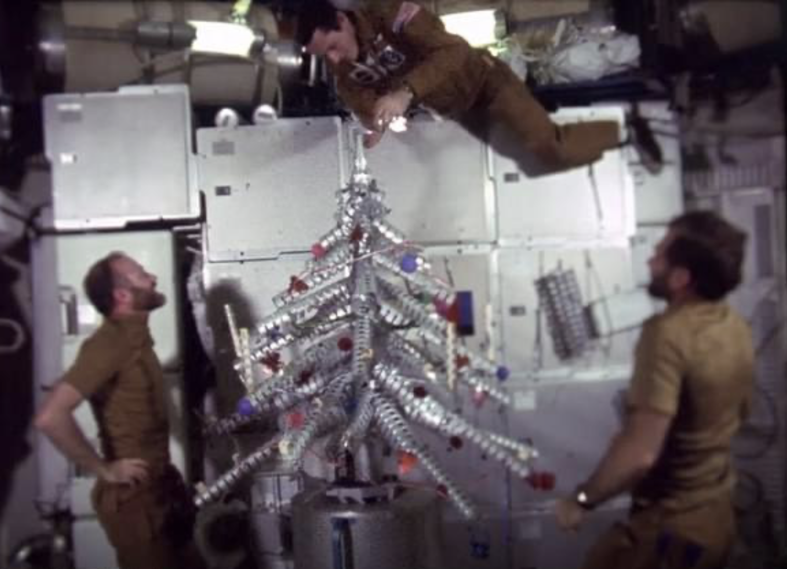 Skylab 4 astronauts Gerald P. Carr, left, Edward G. Gibson, and William R. Pogue build and decorate their makeshift Christmas tree