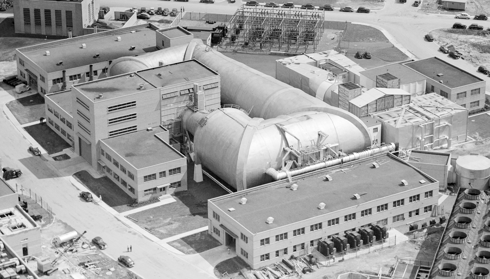 A black-and-white aerial view of a group of buildings at NASA’s Glenn Research Center. A large wind tunnel can be seen at the center of the photo.