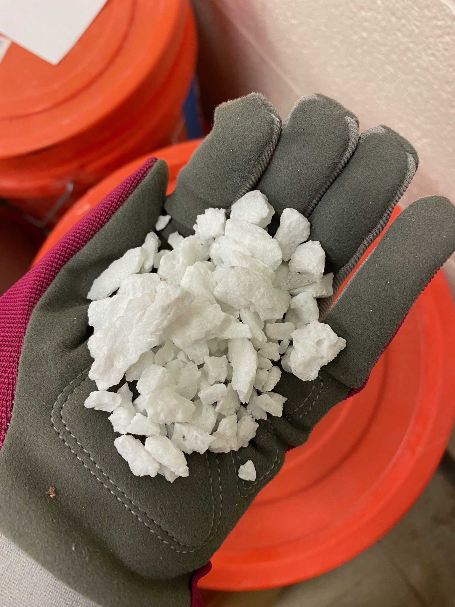A gloved hand holds a handful of white looking synthetic minerals over a orange bucket.