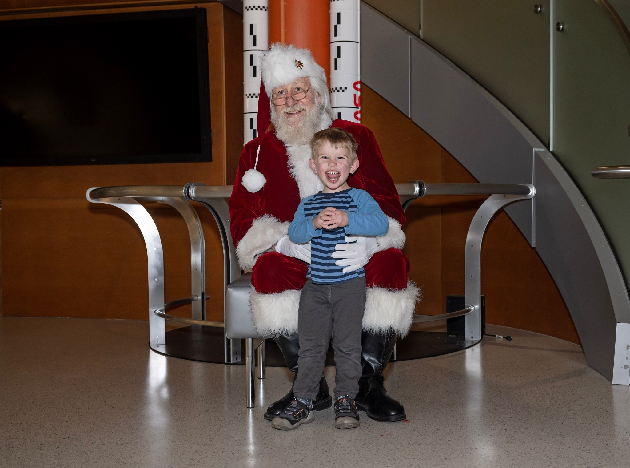 A young boy gleefully gives an open mouth smile after meeting Santa Claus. Children were given the chance to meet and take photos with Santa in the foray of Building 4221. There was also hot chocolate and cookies for attendees.