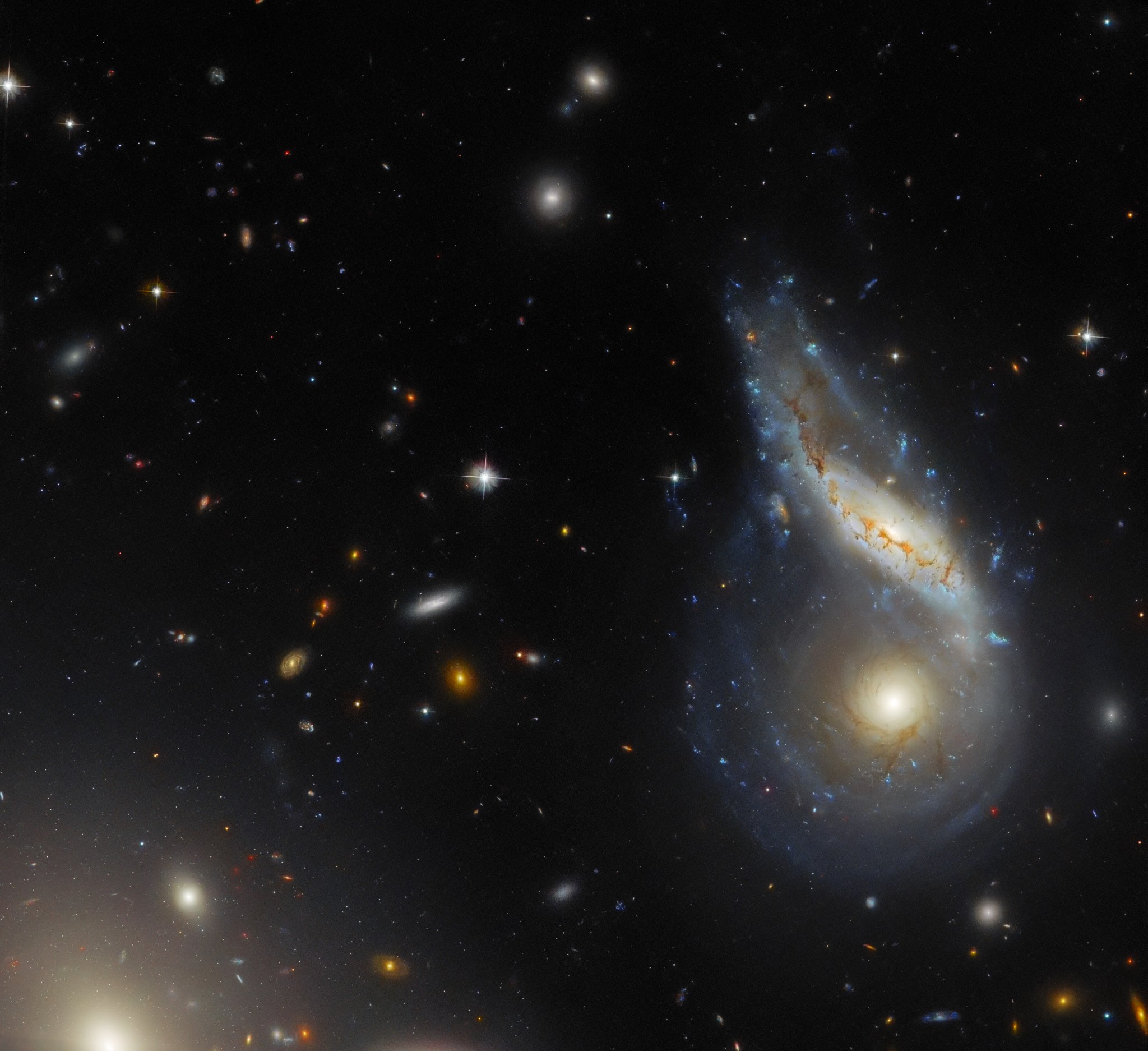 Two galaxies form a teardrop, paisley-like shape at right as they collide. Other galaxies dot the darkness of space.