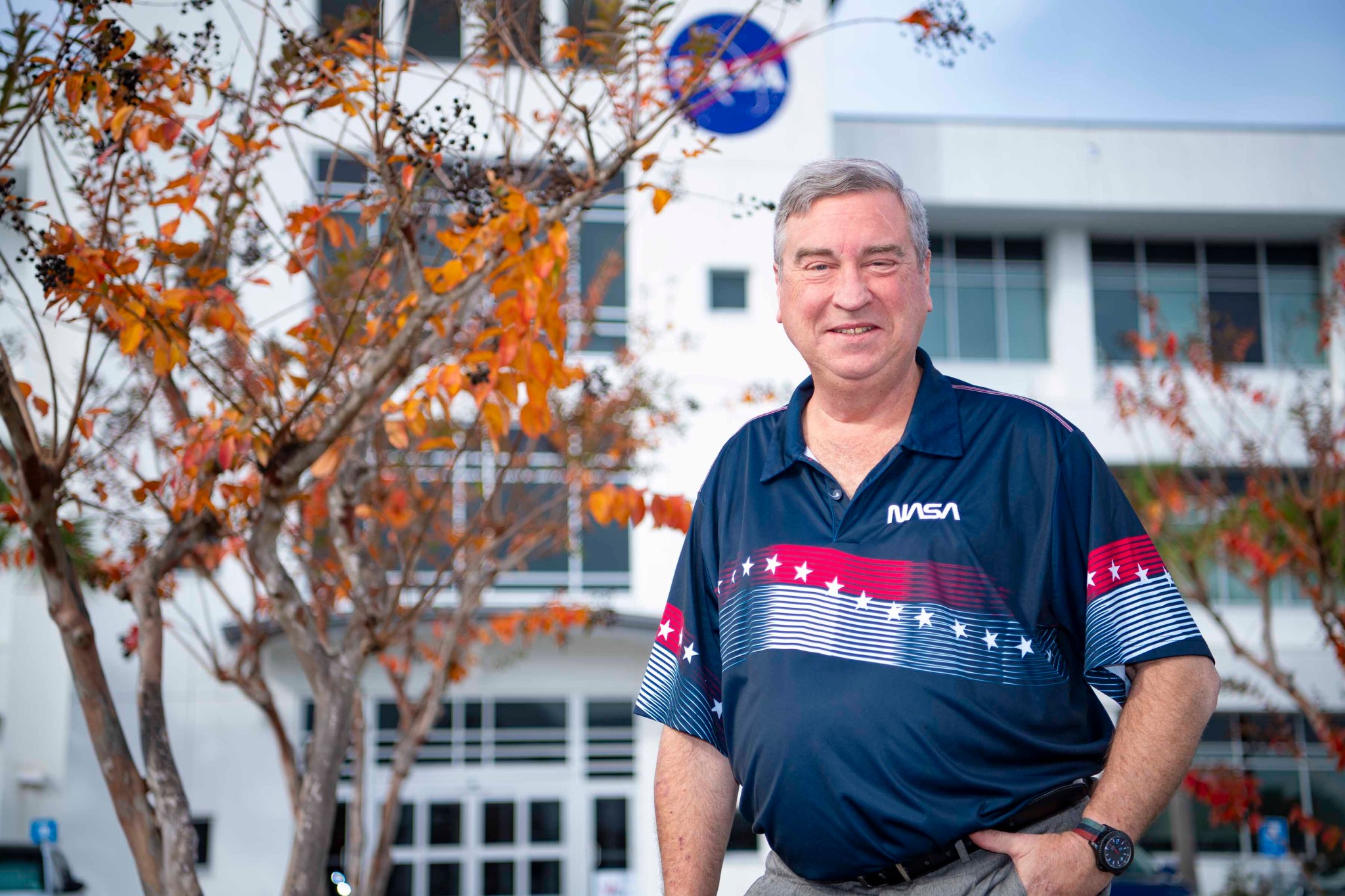 Tony Goretski, wearing a navy NASA polo shirt, smiles at the camera while standing outside of a building at NASA’s Stennis Space Center