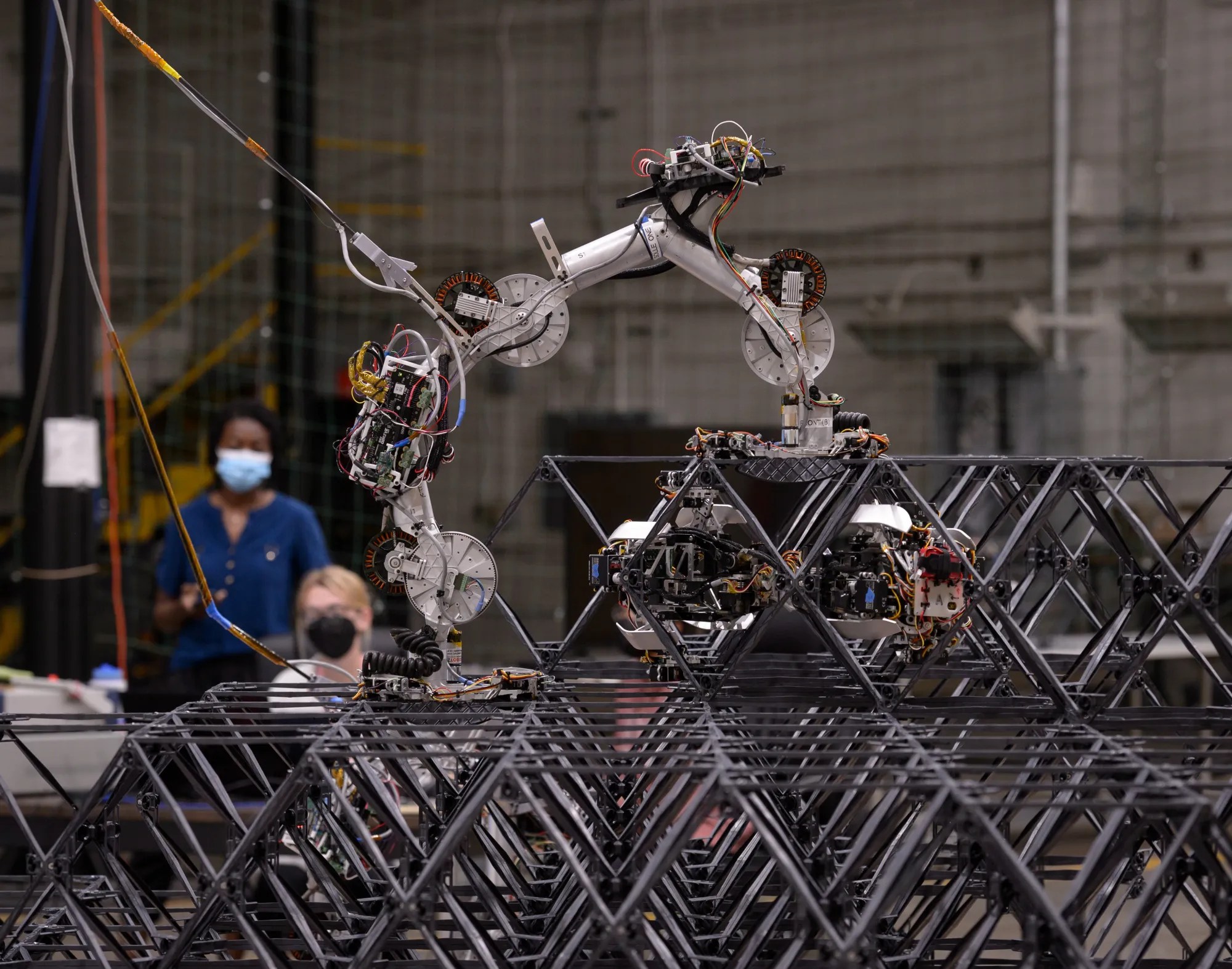 Research engineer Taiwo Olatunde, left, and intern Megan Ochalek, right, observe as robots move and assemble composite building blocks into a structure.