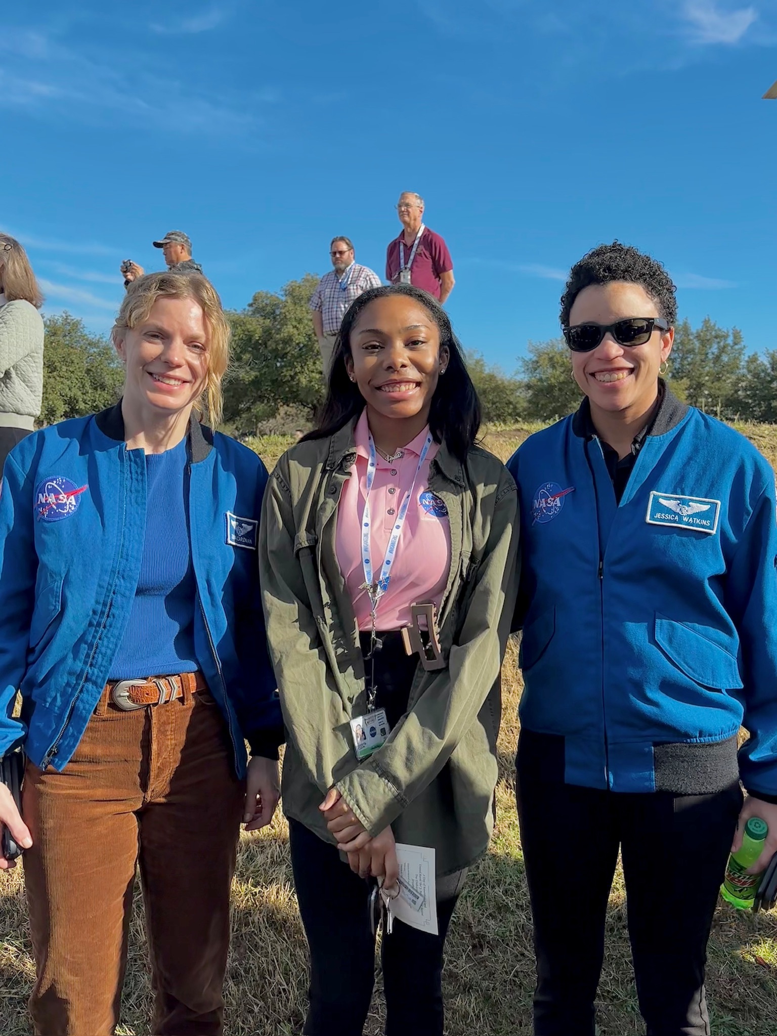 A young woman poses for a photo with two female NASA astronauts outside.