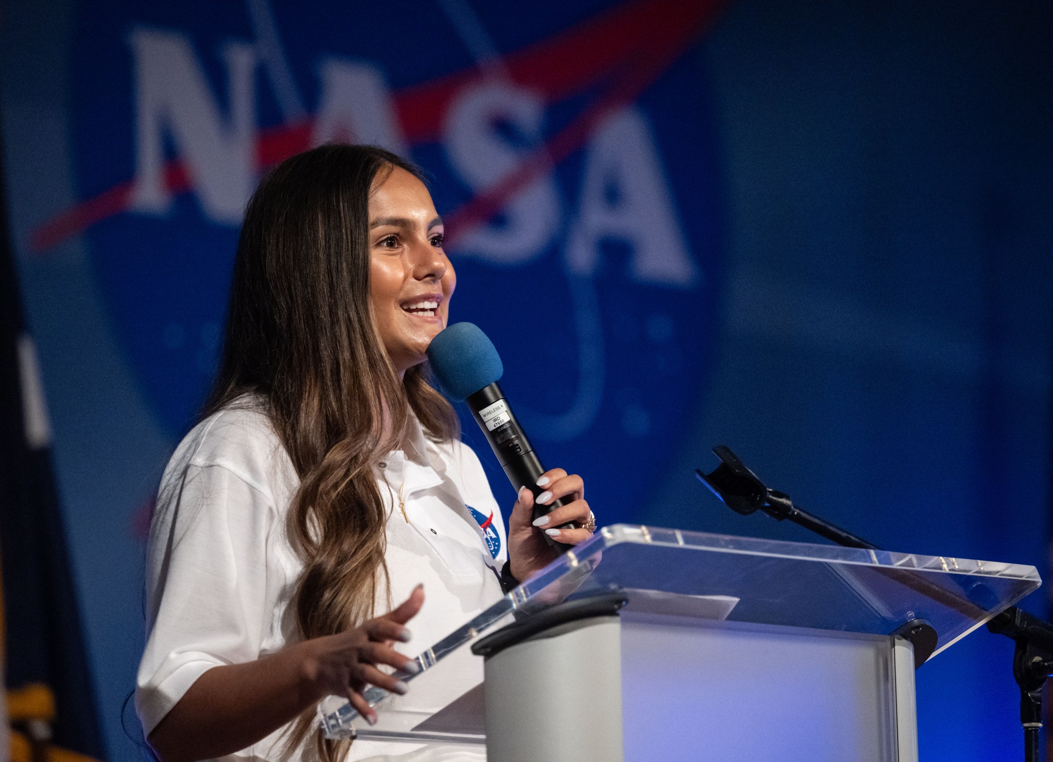 A young woman stands behind a podium and speaks into a microphone.