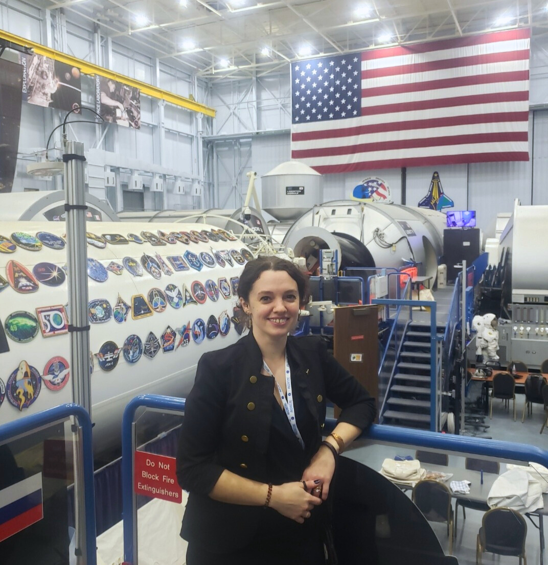 A young woman stands on a raised platform in front of a mockup of an International Space Station Module.