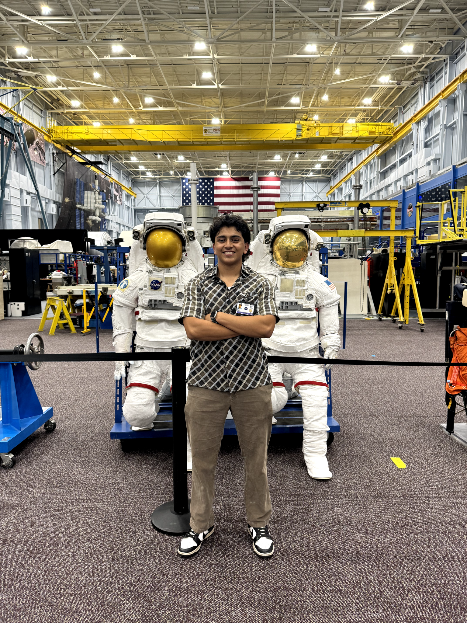 A young man poses for a photo with two spacesuits in the background.