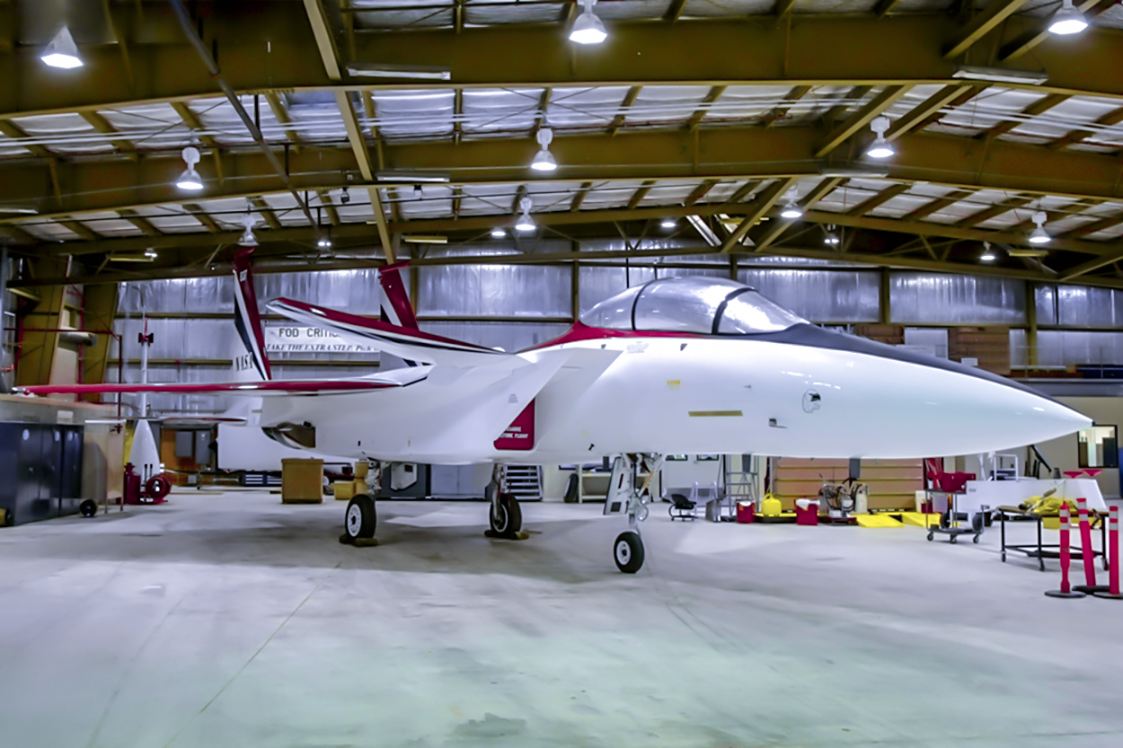 A white fighter jet turned into a research aircraft with red and blue trim is parked inside a NASA hangar.
