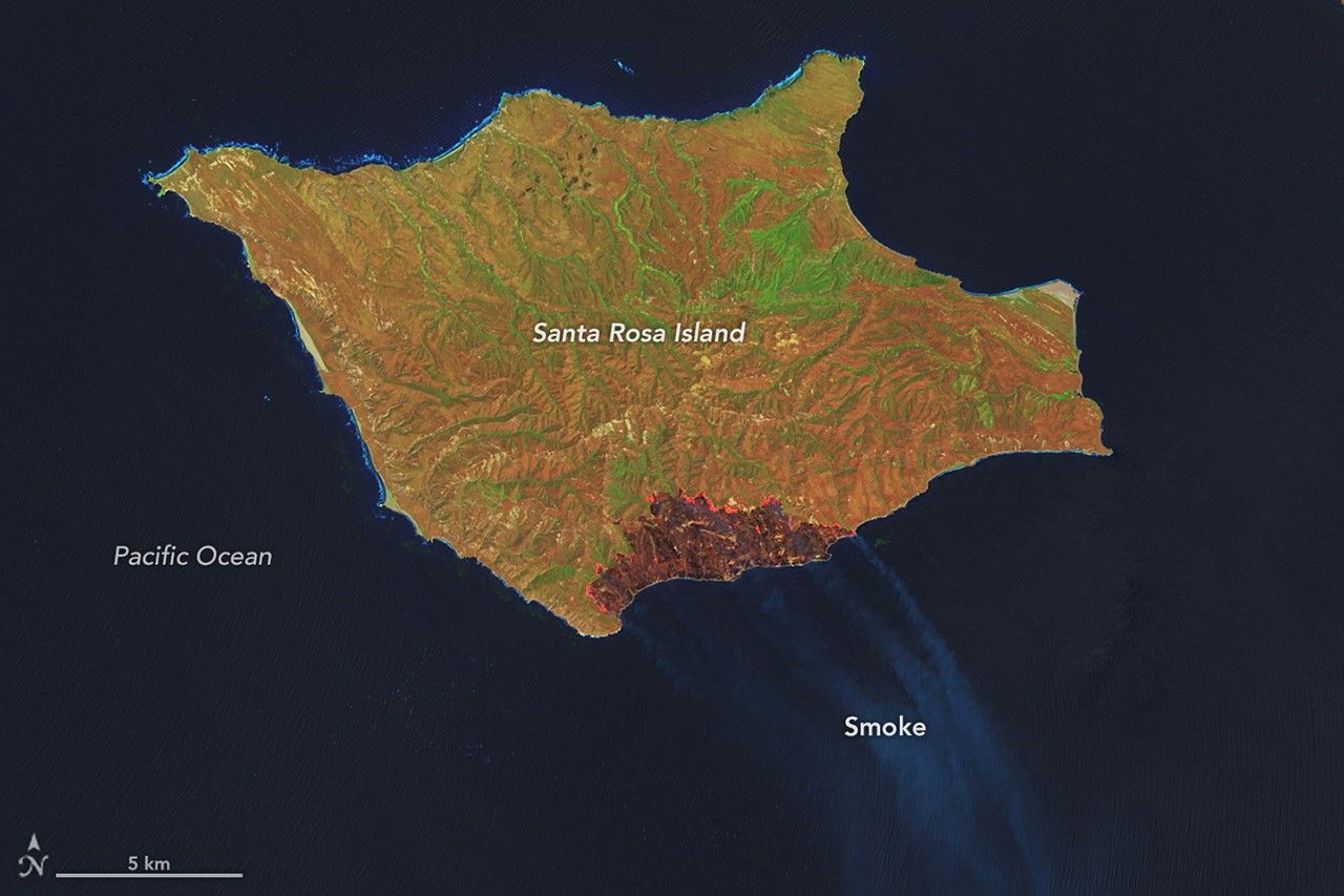 A downward-looking image of Santa Rosa Island shows a dark-brown burned area toward the bottom-right. A thin, bright orange line runs along the burned area, indicating the active fire front.
