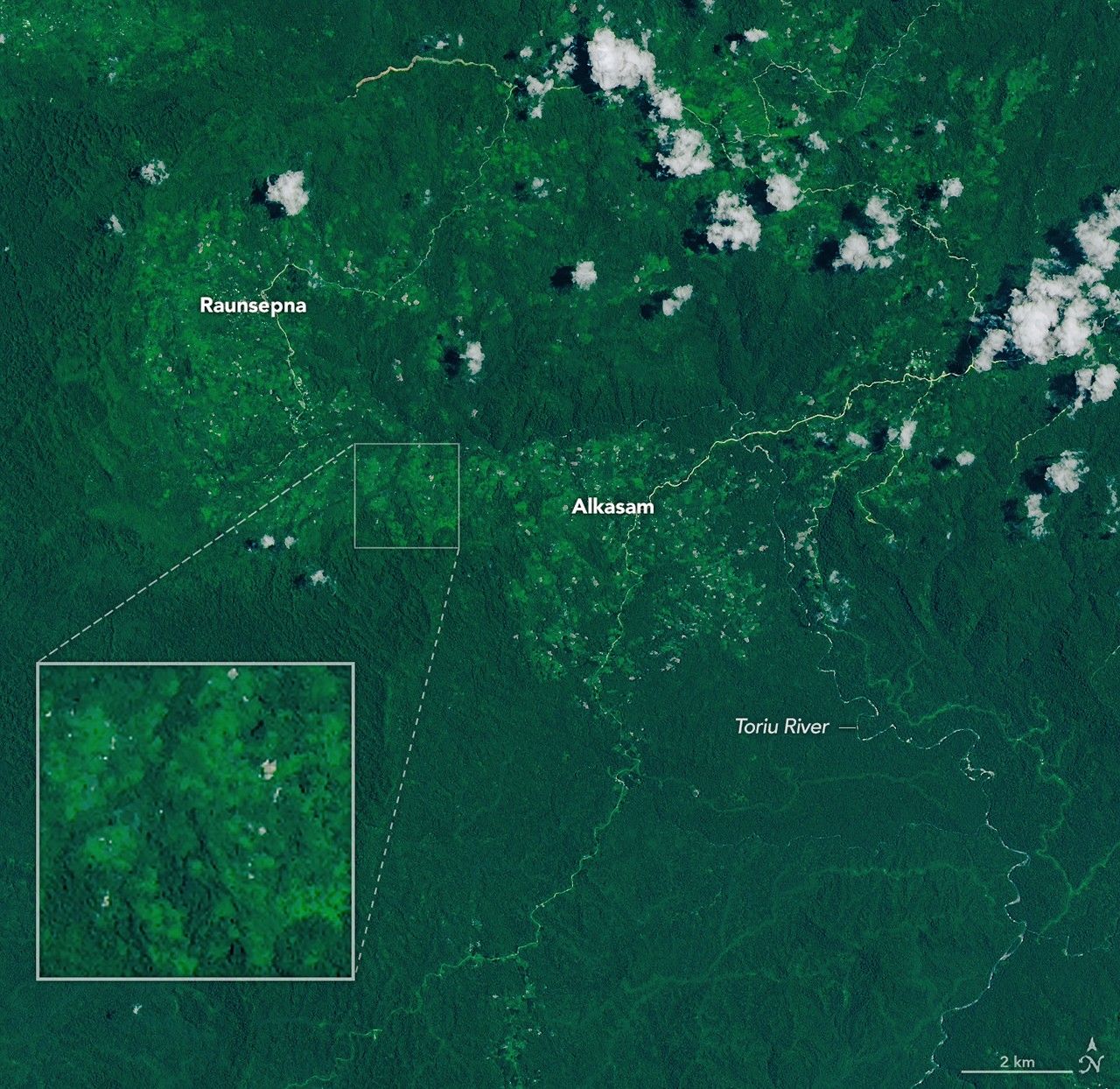 A narrow, light-brown landslide scar cuts through dark green forested mountains in East New Britain and extends south toward a stream valley. Rivers swollen with floodwaters, areas of forest clearing, and scattered clouds are also visible in some parts of the image.