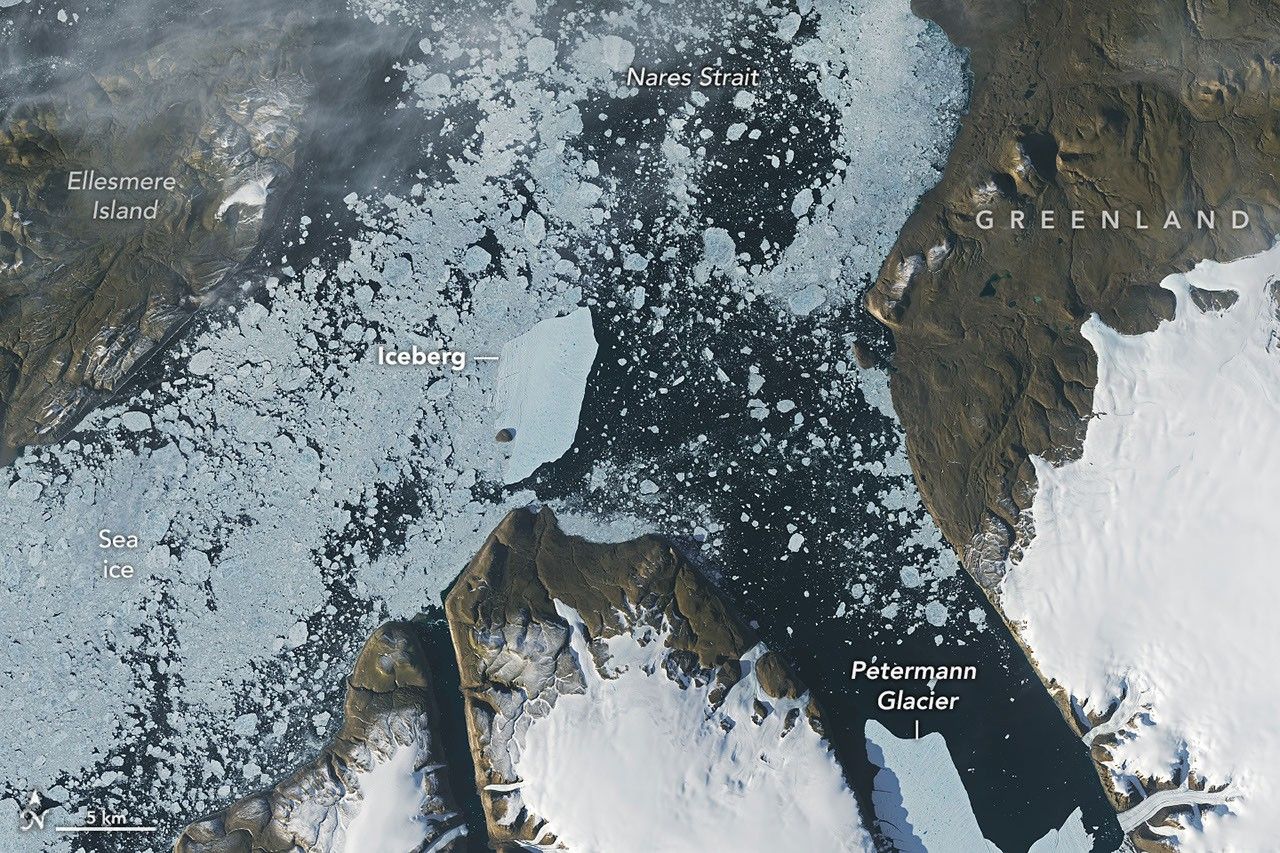 A satellite view shows the iceberg after it pivoted out of the fjord into Nares Strait, wedged against a small, brown island.